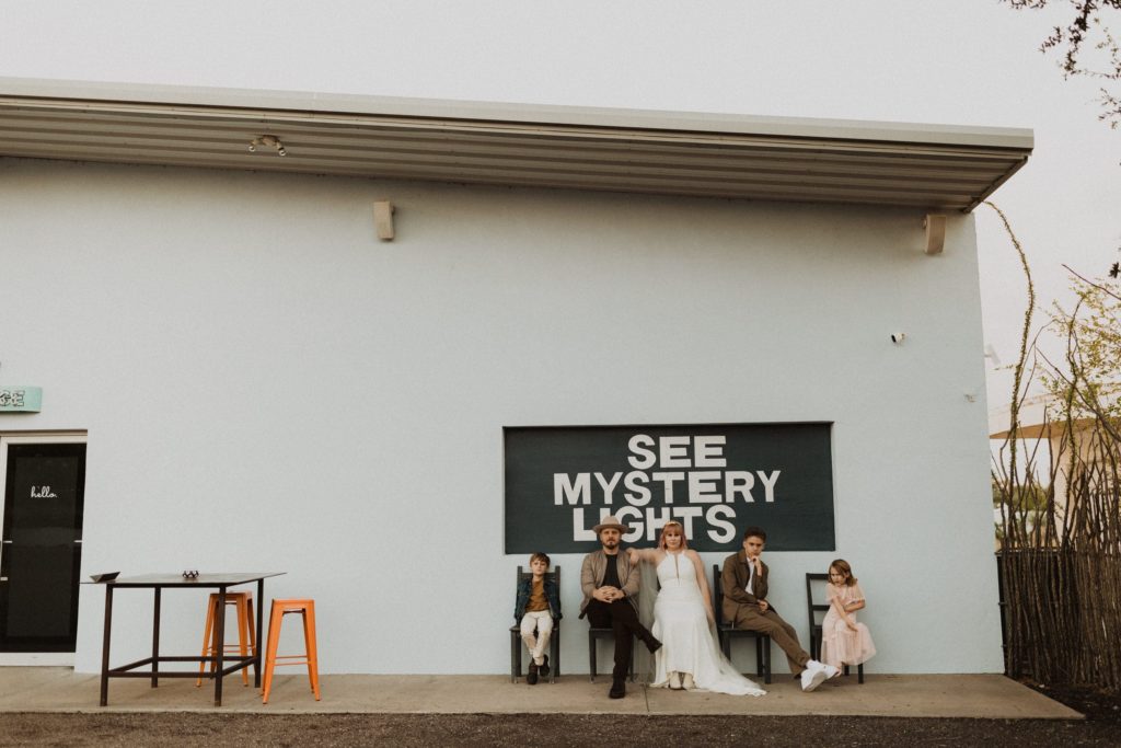 Family sitting in front of see mystery lights sign during their Marfa Texas elopement