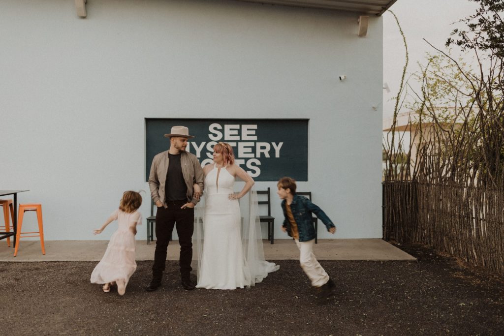 Bride and Groom look at each other while their kids run around in front of the see mystery lights sign in Marfa Texas during their Marfa Texas Elopement