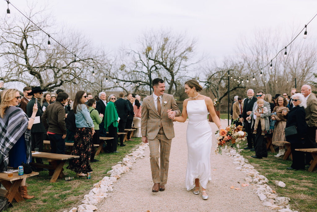 couple holds hands walking down aisle at Camino Real Ranch wedding 