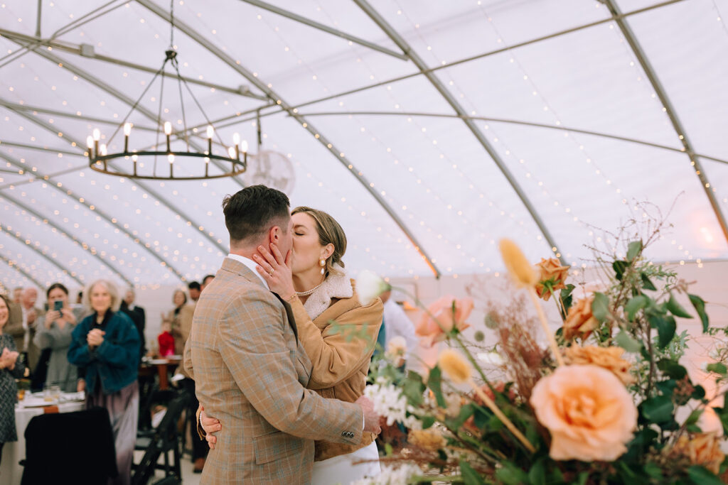 couple kisses in front of floral wedding table