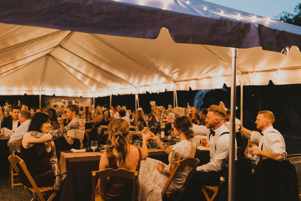 couple cheers at tented wedding reception