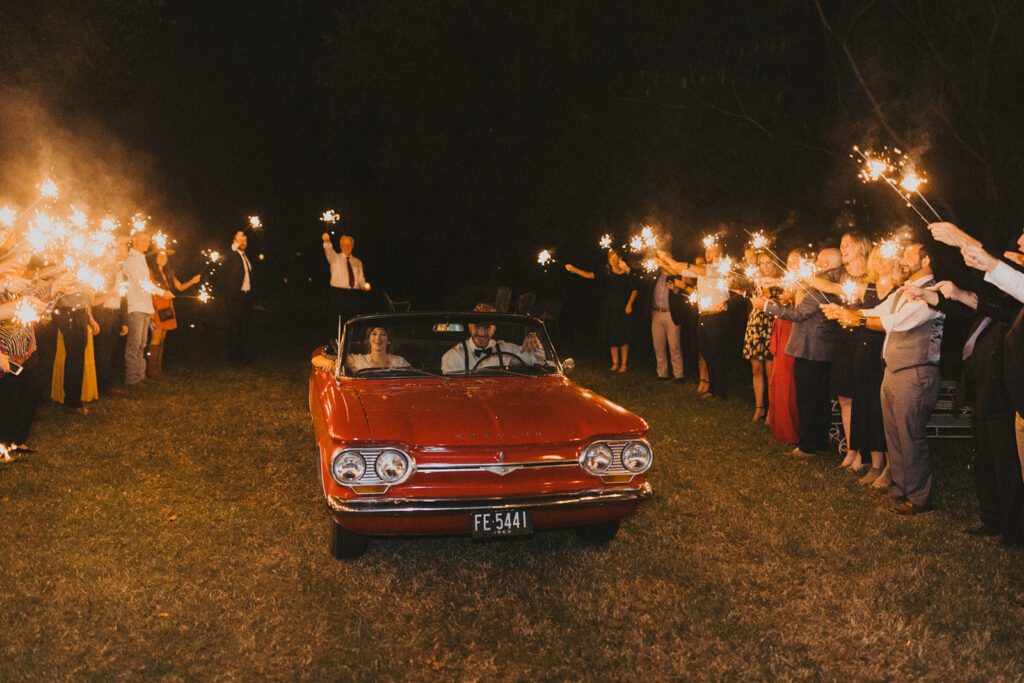 couple drives in red car to sparkler wedding exit