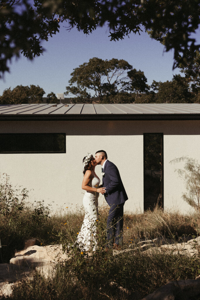 couple kisses in front of house in woods in Central Texas