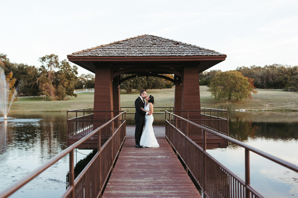 couple kisses on dock over lake at outdoor Central Texas wedding