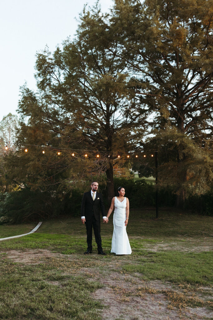 couple holds hands under twinkle lights at outdoor wedding