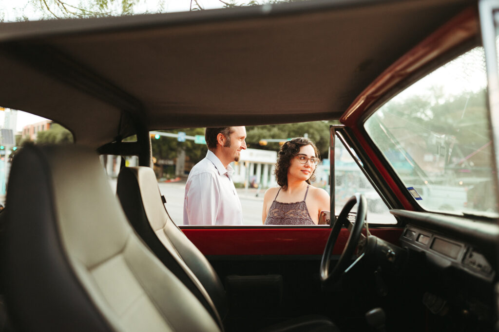 couple stands beside red car for urban engagement session