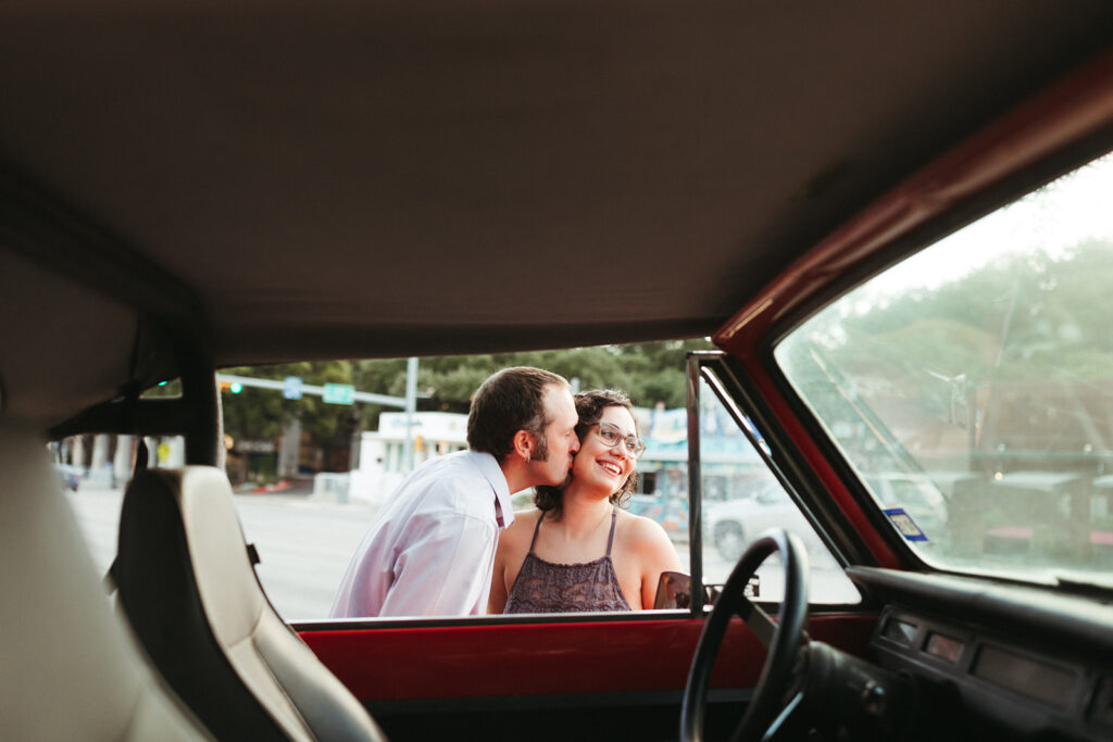 couple kisses beside red car for urban engagement session