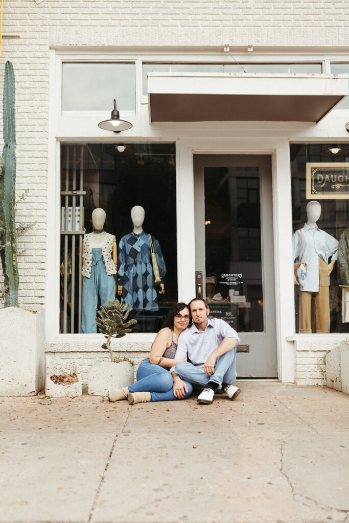 couple sits on ground in front of shop