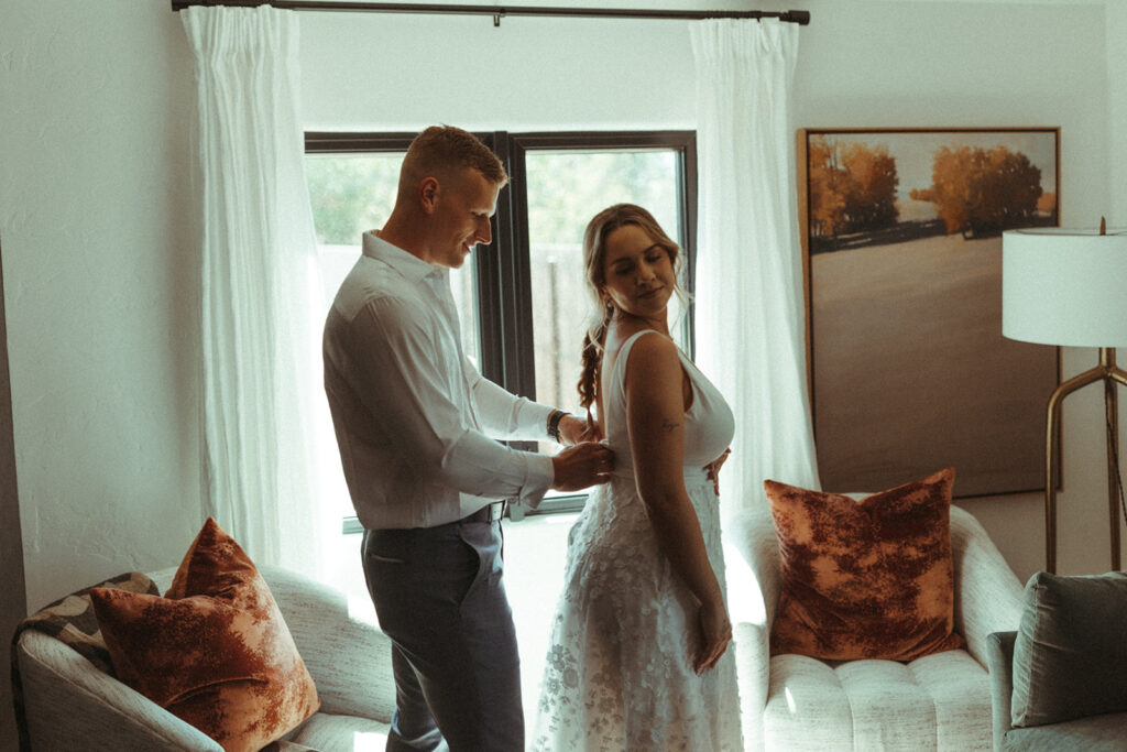 groom zips up bride while getting ready together