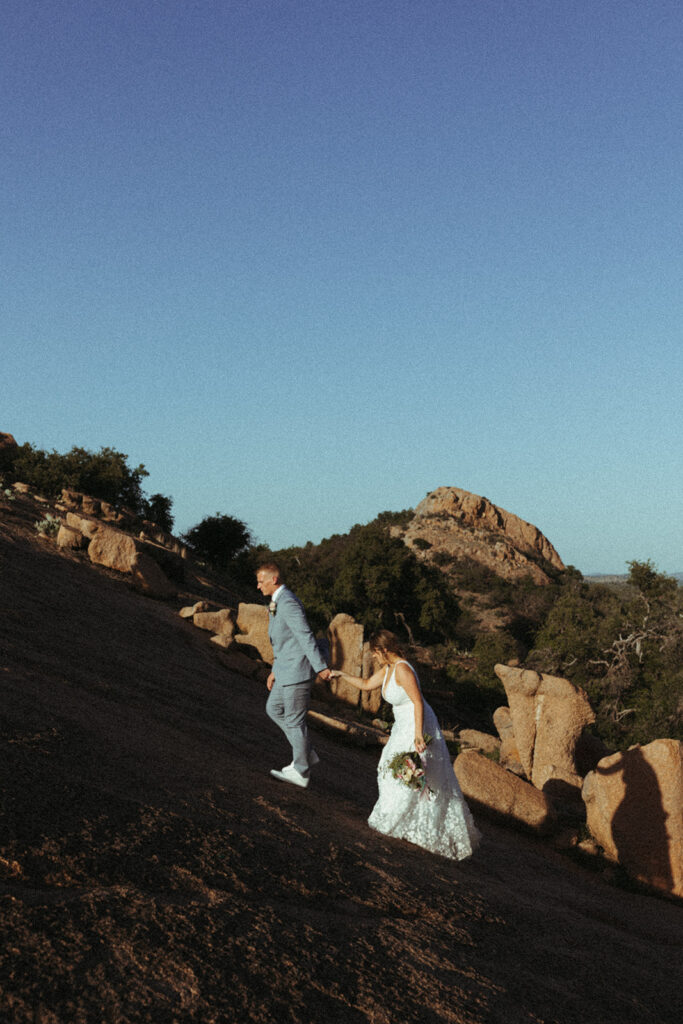 couple holds hands walking up enchanted rock at sunset elopement