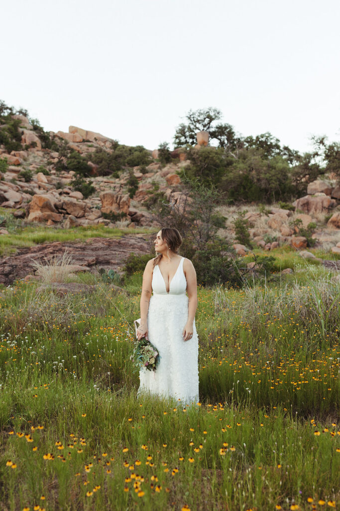 bride stands in wildflower field at enchanted rock sunset elopement