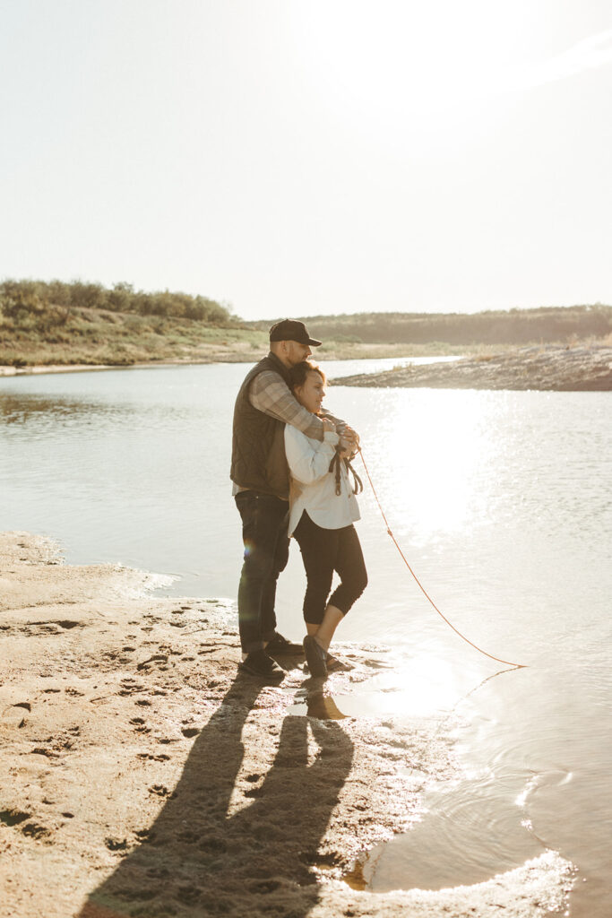 couple embraces at beside lake at sunrise elopement
